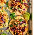 Vegetarian chickpea tacos topped with crispy roasted chickpeas, black beans, cauliflower, purple cabbage, and green avocado salsa on a sheet pan.