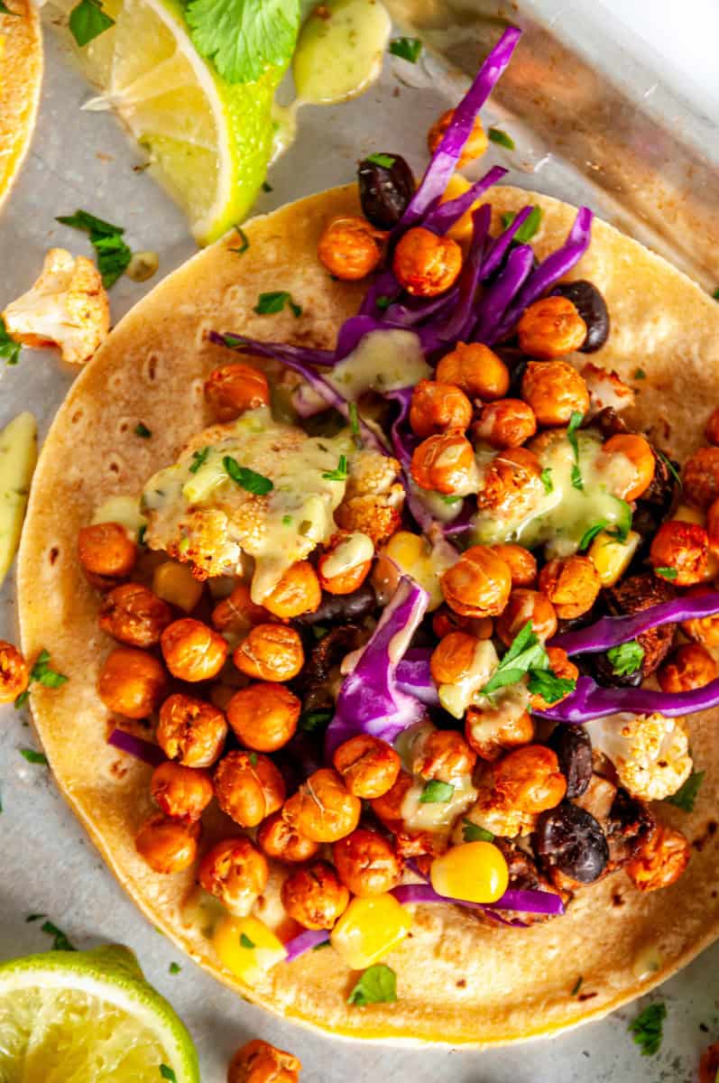 Close-up of a vegetarian chickpea taco with crispy roasted chickpeas, roasted cauliflower, black beans, corn, and creamy green avocado sauce.