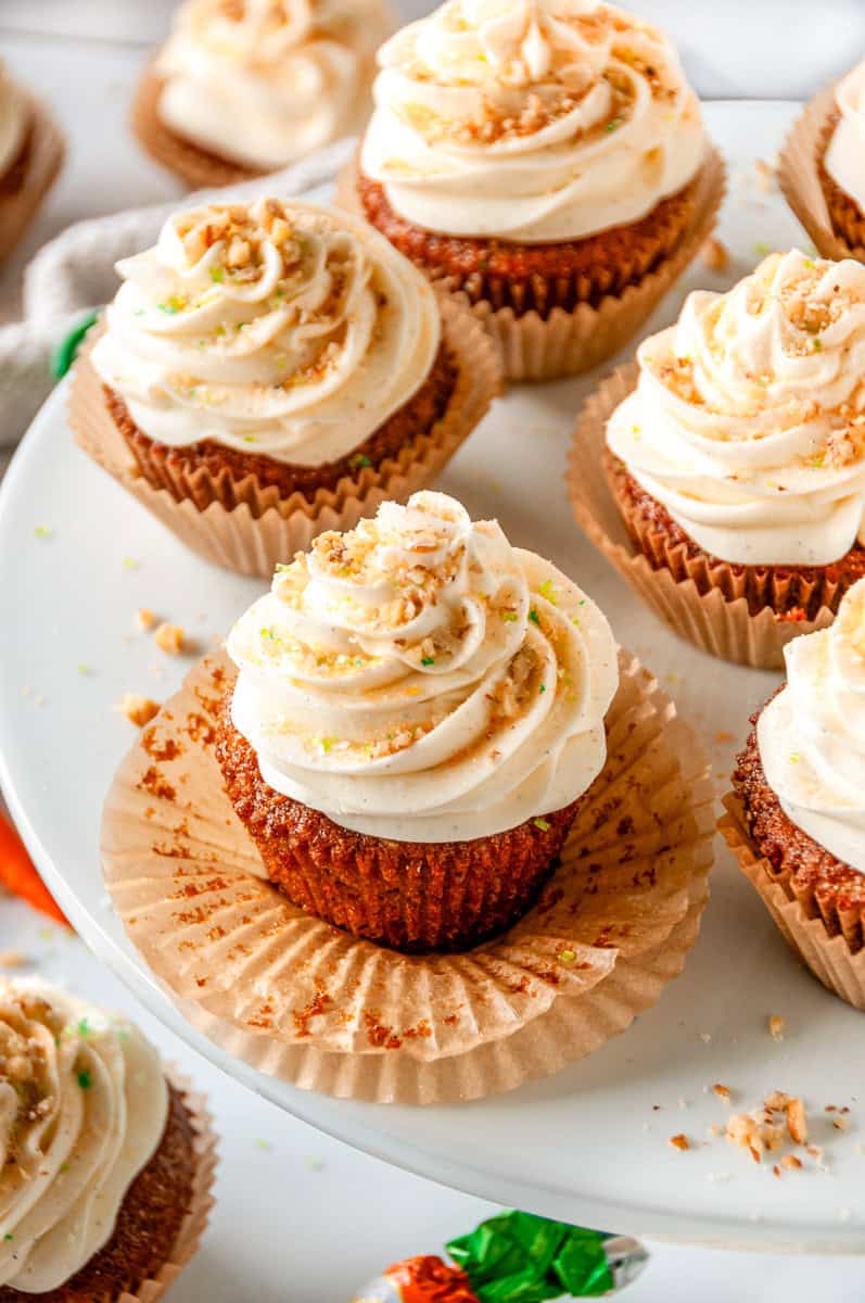 Carrot Cake Cupcakes arranged on a white cake stand with cream cheese frosting and festive sprinkles