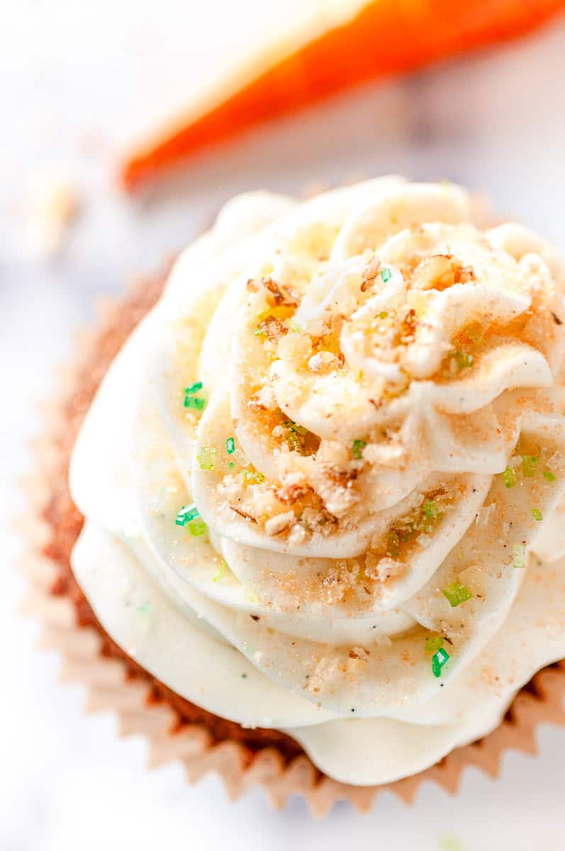 Overhead close up of Carrot Cake Cupcake frosting swirl with chopped nuts and colorful sprinkles