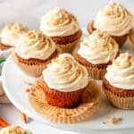 Carrot Cake Cupcakes with cream cheese frosting on a white cake stand, topped with chopped nuts and sprinkles