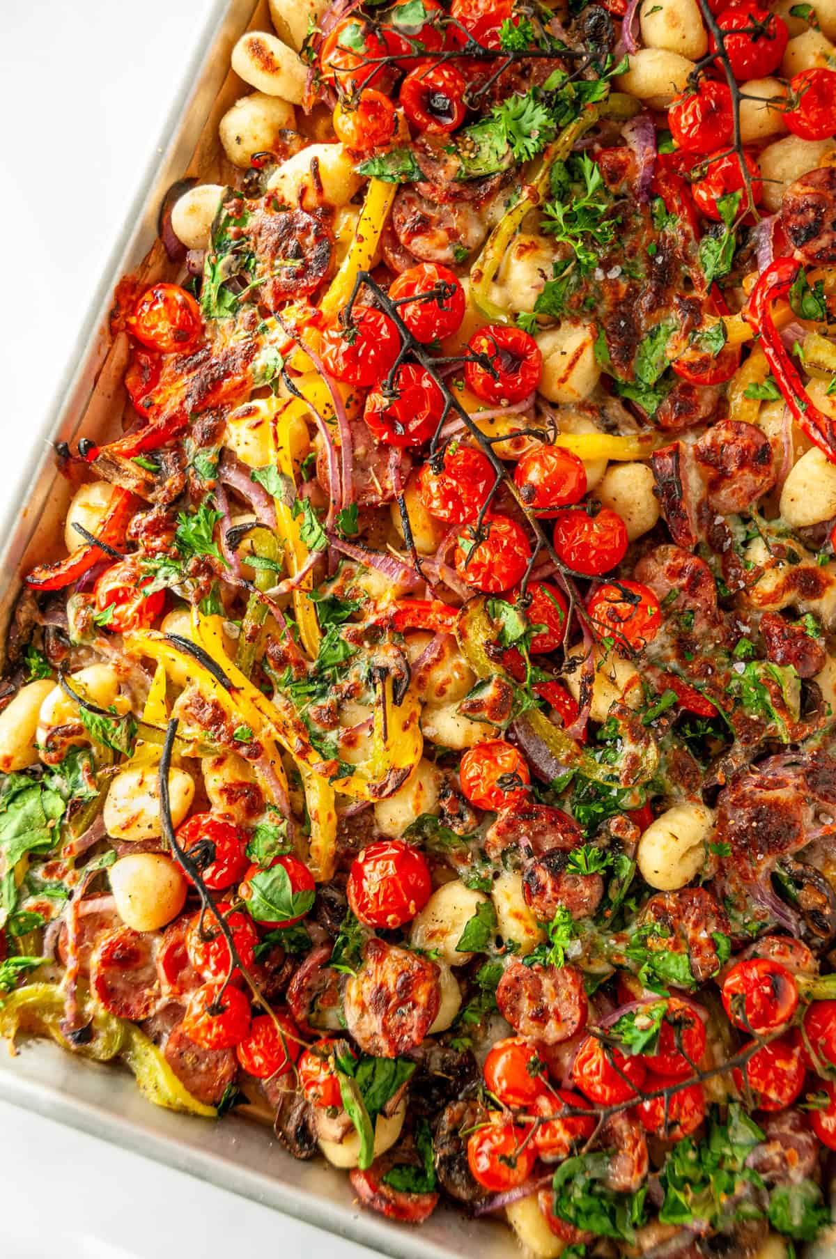 Close-up of sheet pan sausage gnocchi with crispy gnocchi, turkey sausage, roasted vegetables, and melted cheese.