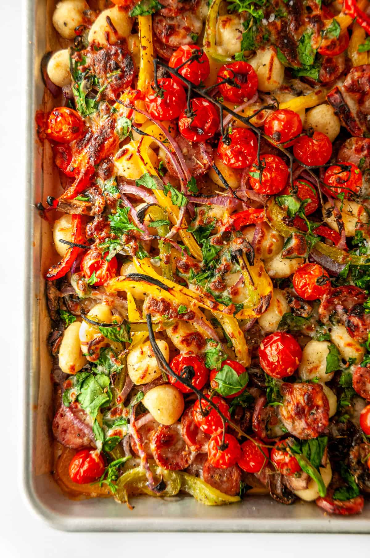 Close-up of finished sheet pan sausage gnocchi with blistered tomatoes, turkey sausage, melted cheese, and fresh herbs.