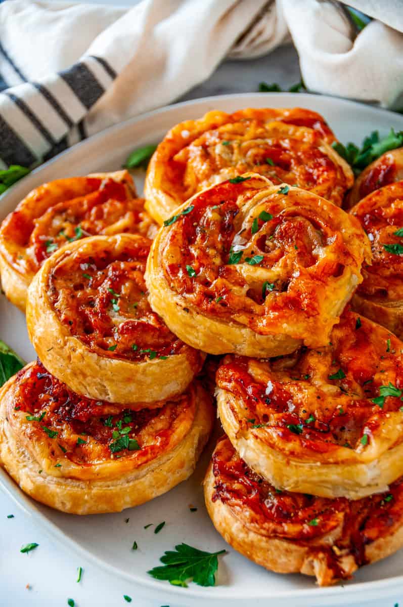 Golden brown ham and cheese pinwheels on a plate, topped with fresh parsley and showcasing flaky puff pastry layers