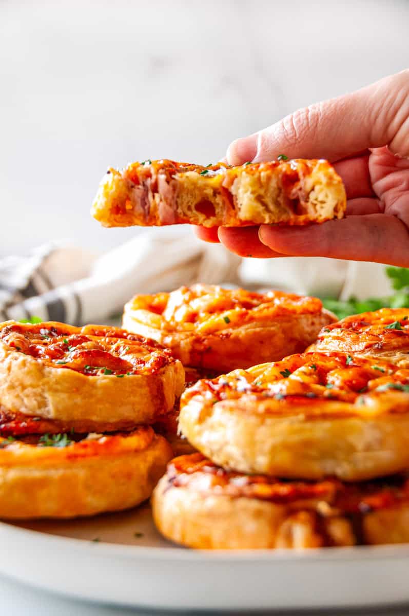 Hand holding a piece of ham and cheese pinwheels showing flaky texture and cheesy filling inside