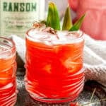Jungle Cat cocktail with a whole pineapple, a bottle of Ransom, and a pink ceramic cat on a white marble counter.